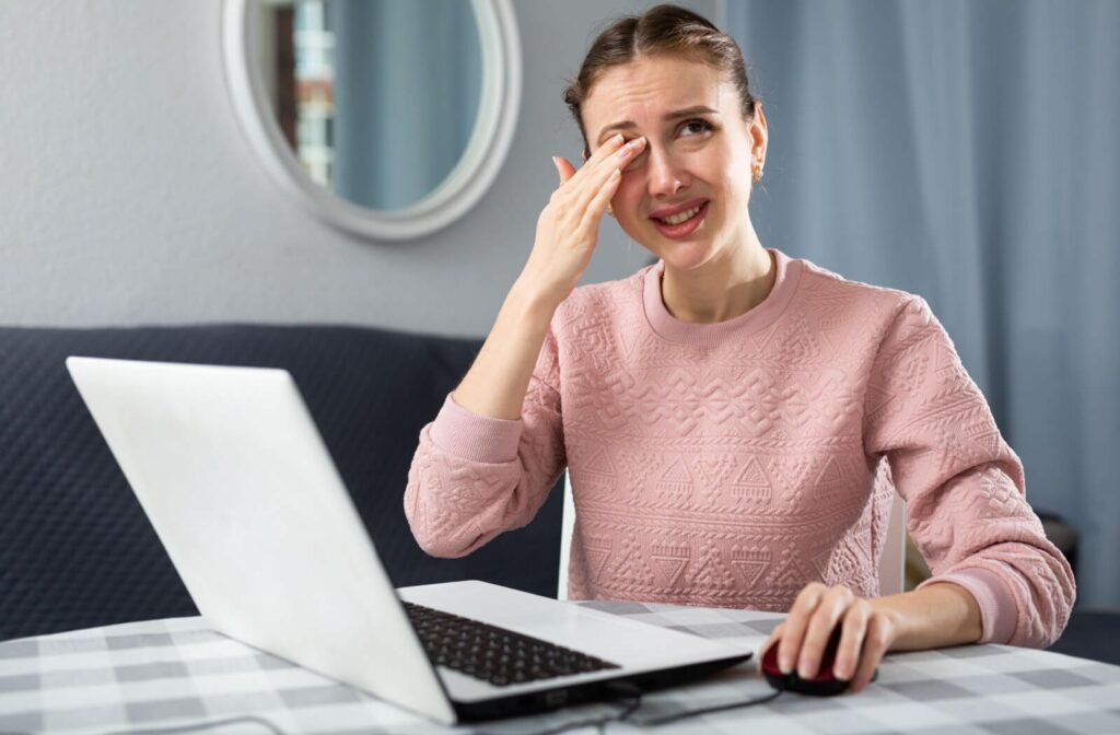 Young woman in distress and experiencing eye pain after long exposure to a computer screen.