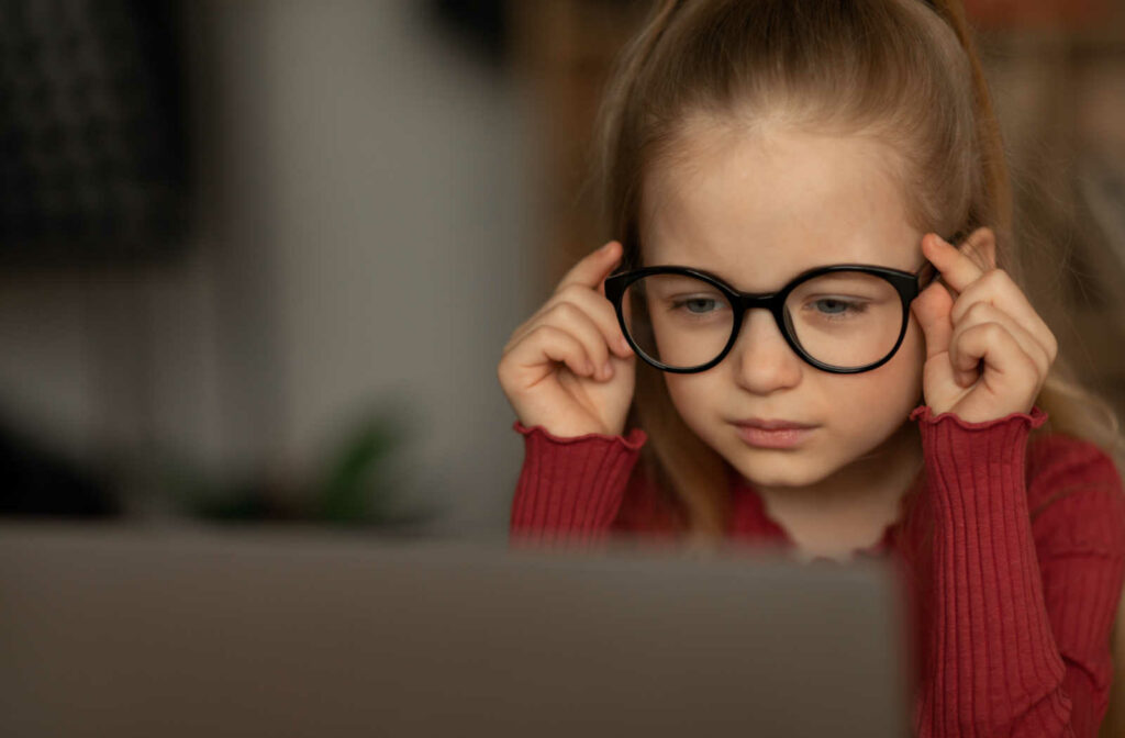 A child wearing glasses and looking closely at a laptop