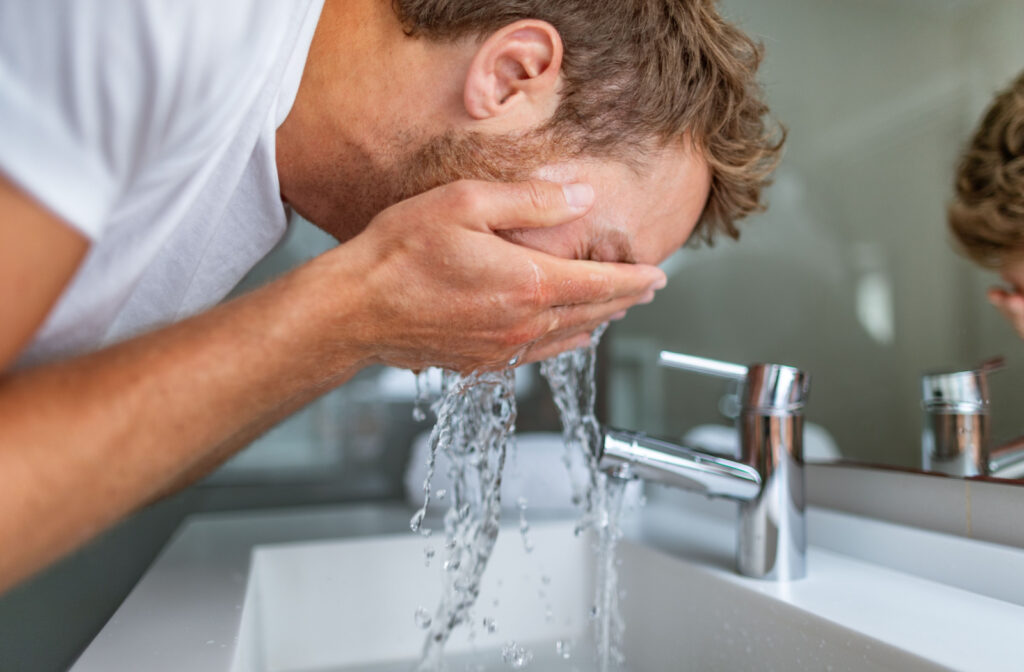 A man rinsing his eyes with clean water to try and get sunscreen out.