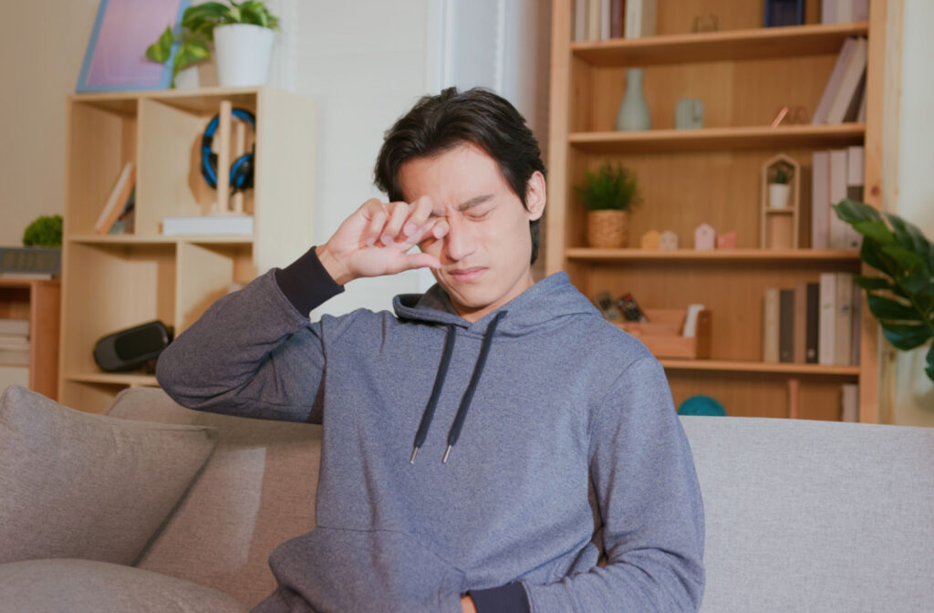 A man sitting on the couching rubbing his eye with the bad of his hand.