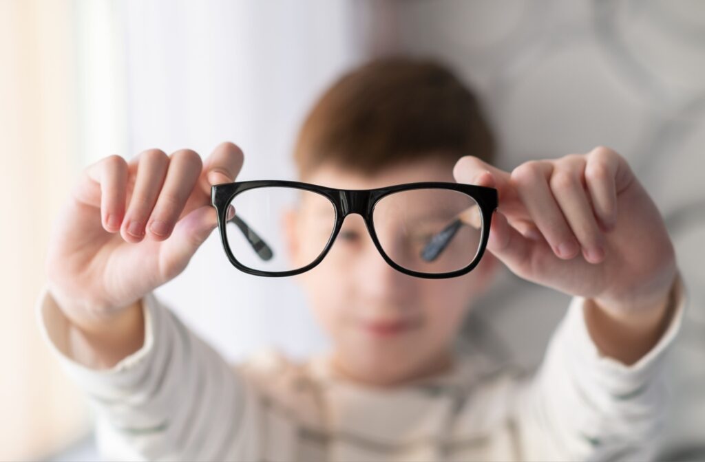 A young boy holding a pair of eyeglasses straight out in front of his face.