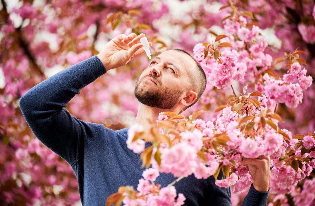 A man put drops in his eyes while surrounded by lush, pink tree blossoms.