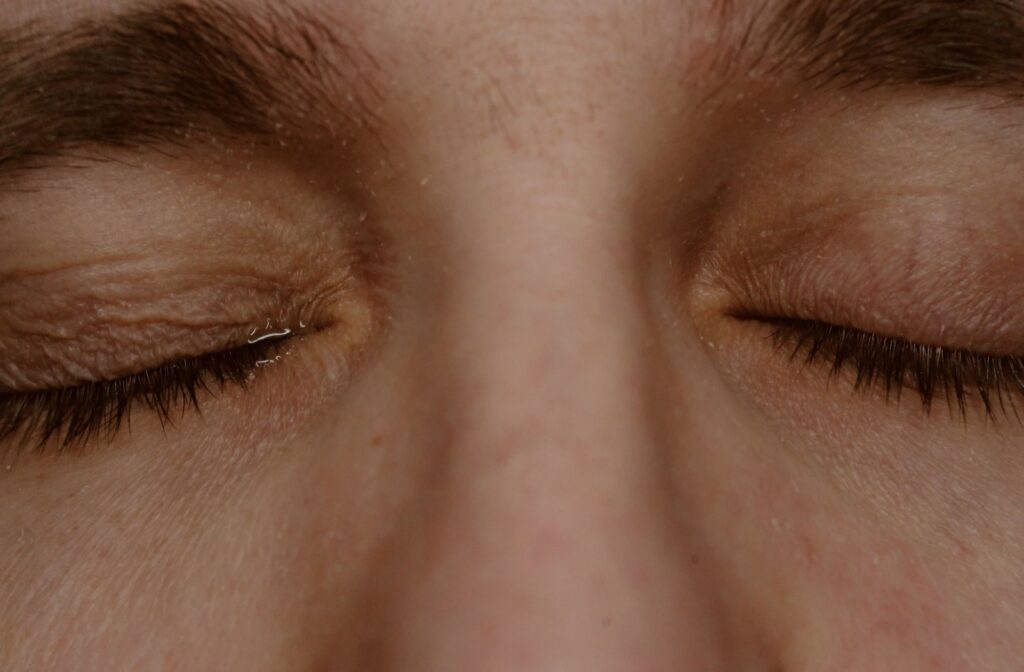 A close-up of a person with their eyes shut, and a single tear peaking through.