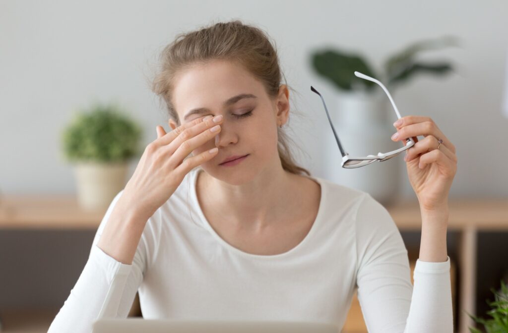 A woman taking off her glasses and rubbing her dry eyes.