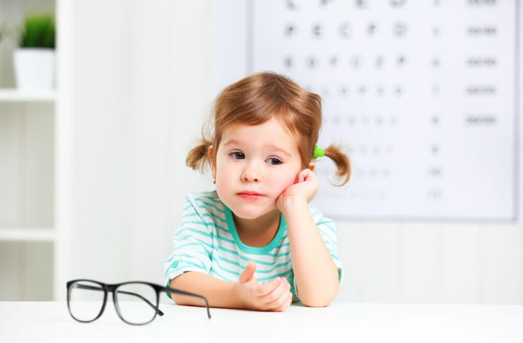 A bored-looking child sits next to a pair of glasses in an optometrist's office.
