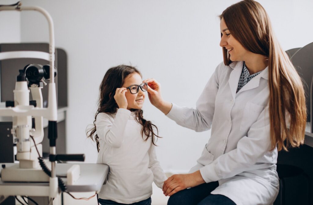 Optometrist smiling at young patient helping her put on new myopia glasses.