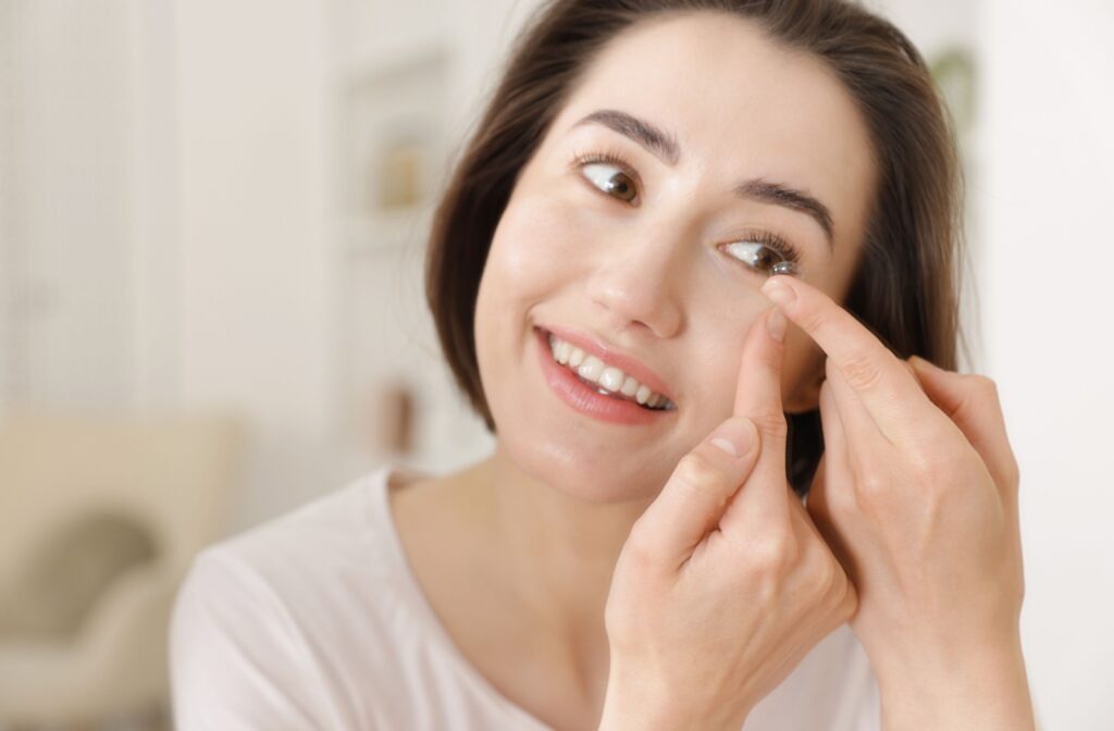 A person looking in the mirror and smiling as they put a contact lens into their eye