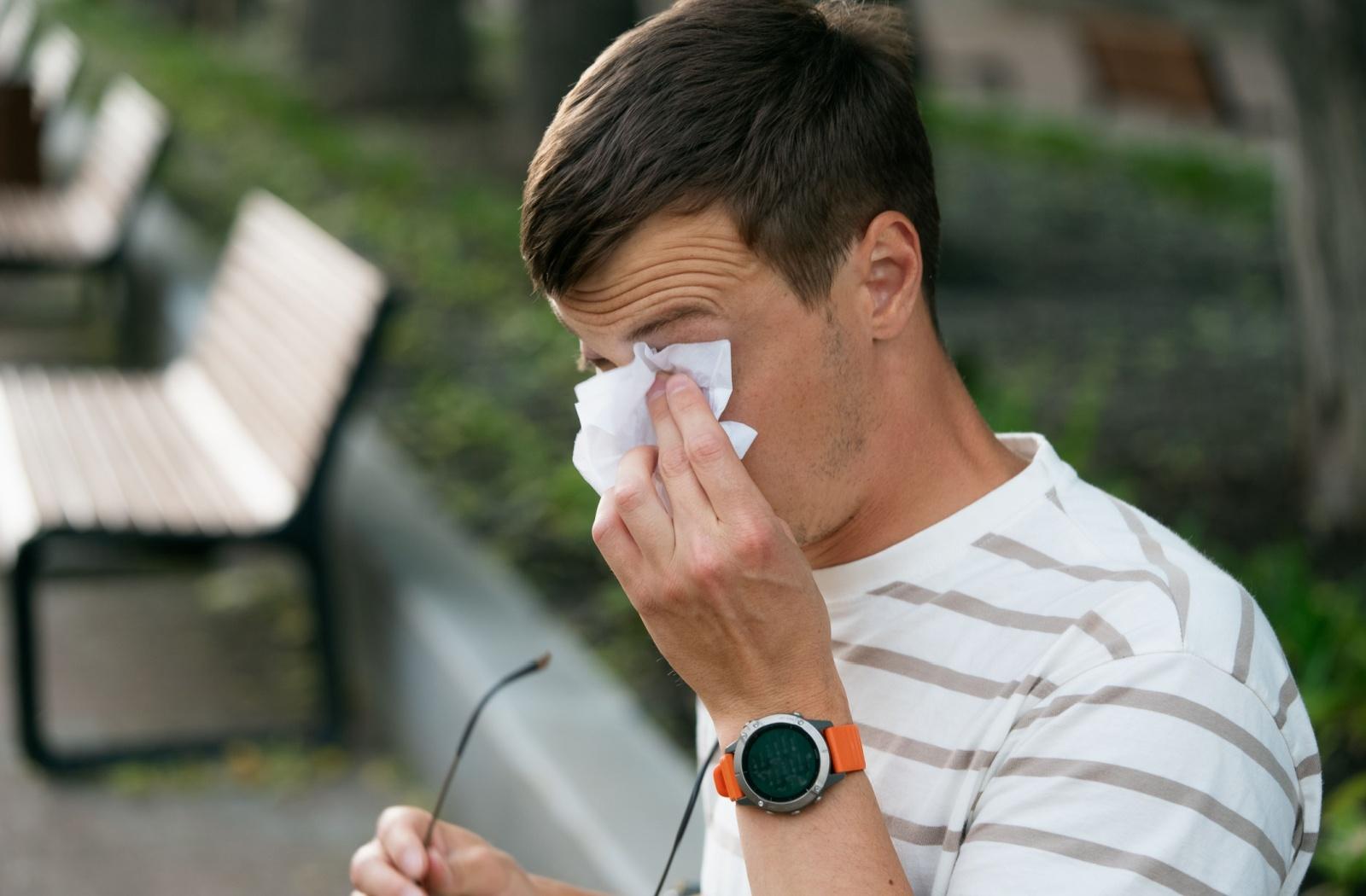 A person rubbing their eye with a tissue as they experience eye allergies